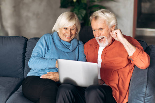 istock Elderly modern spouses communicate by video call using a laptop with family or friends while sitting at home on the couch and waving their hands to the camera 1286546464