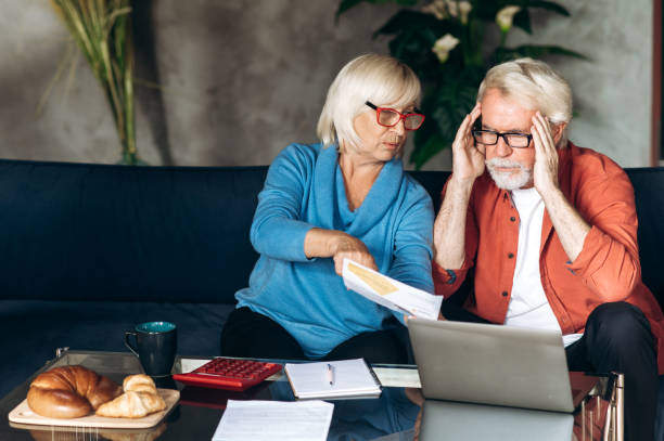 istock Online bill payment. Mature sad retirees count and pay their utility bills using calculator and laptop while sitting on a sofa at home 1286546468