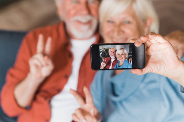 istock Modern old people. Caucasian elderly couple taking selfie on mobile phone while sitting on sofa and smiling 1286546472