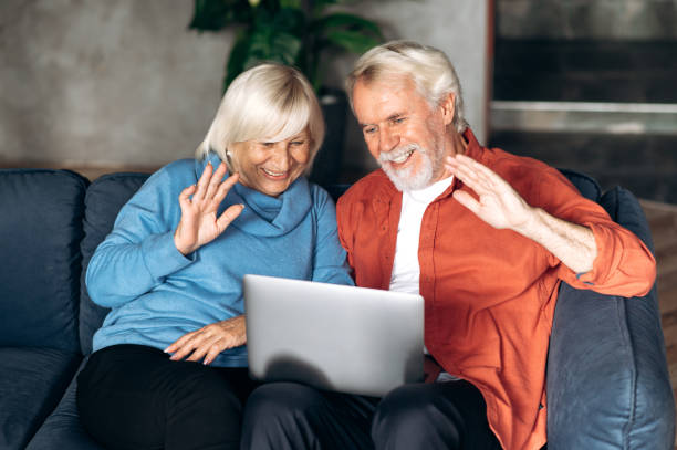 istock Elderly modern spouses communicate by video call using a laptop with family or friends while sitting at home on the couch and waving their hands to the camera 1286546474