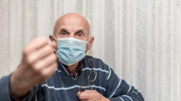 angry aggressive elderly man wearing face mask showing big fist self isolation and coronavirus concept angry aggressive elderly man wearing face mask showing big fist self isolation and coronavirus concept white background aggression stock pictures, royalty-free photos & images