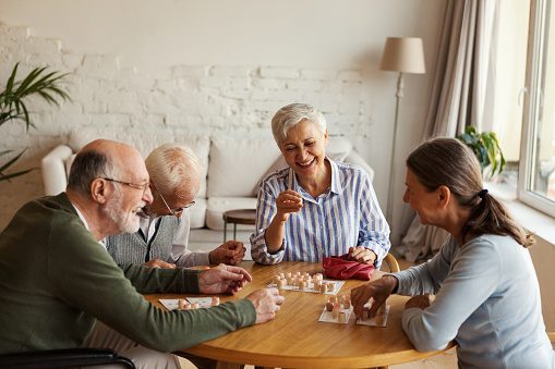Grupo de cuatro personas mayores alegres, dos hombres y dos mujeres, divirtiéndose sentados a la mesa y jugando al bingo en el asilo de ancianos photo