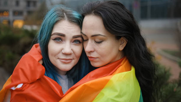 istock Lesbian couple hugging covered with rainbow flag in public 1286546825