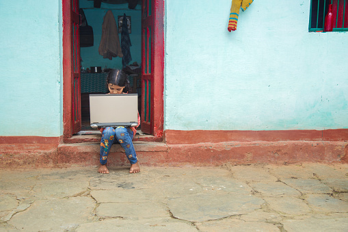 Indian village girl operating laptop computer system seating at home corridor