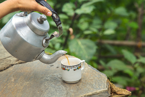 Hand holding old teapot, pouring hot tea into a cup, Traditional tea in afternoon.