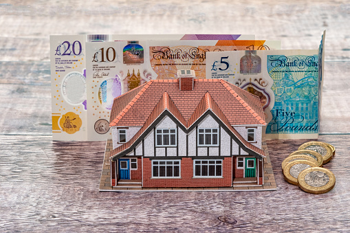 A miniature model house standing in front of UK pound banknotes
