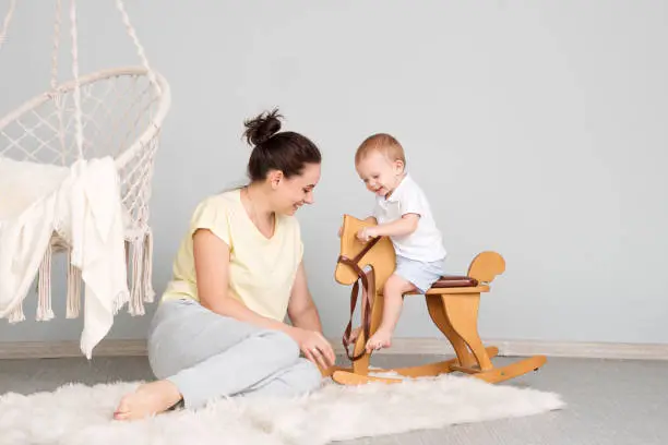 Tender Mom And Son. Child Sitting On Ride On Toy In Playroom. Toddler Baby Boy Riding Swinging On Rocking Chair Toy Horse.