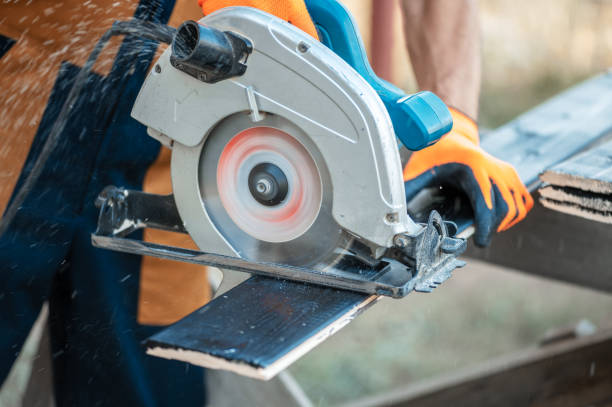 istock Carpenter in overalls saws a black-painted Board with a circular saw, close-up. 1286558323