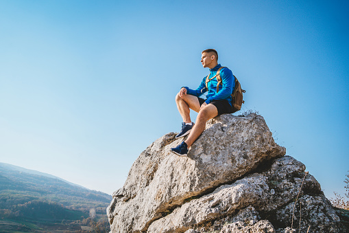 Young caucasian man sitting at the top of mountain and looking at view
