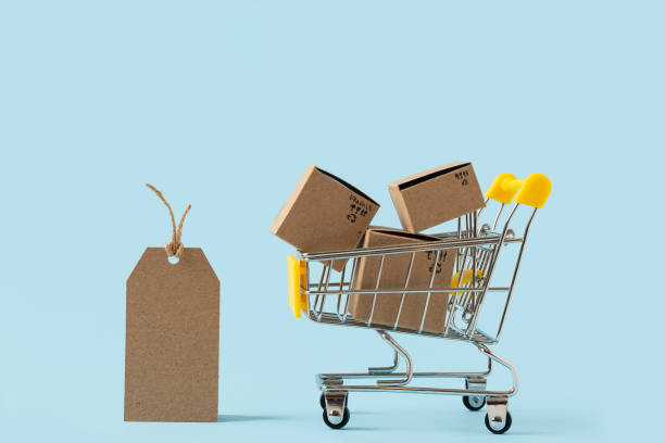 istock Toy shopping cart with boxes and empty tag on blue background. Copy space for text or design. Sale, discount, shopping and delivery concept. Consumer society trend. 1286560237
