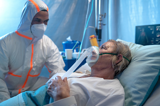 Doctor or healthcare worker talking to covid-19 infected patient in bed in hospital, coronavirus concept.