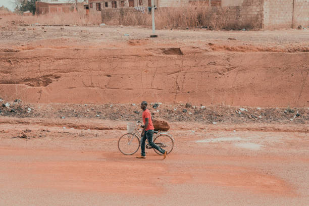 Ouagadougou, Burkina Faso, December 2017. The capital of the sub-Saharan state is the largest city in the country. But the overall poverty of Burkina Faso represents an obstacle for the construction of efficient and fast communication routes. For this reason the roads are in most cases dirt and are crossed by people on foot or by bicycle. In this image you can see a person walking in one of the streets on the outskirts of Ouagadougou.