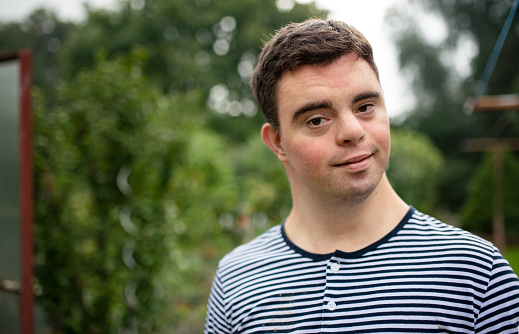 Front view portrait of down syndrome adult man standing outdoors in garden.