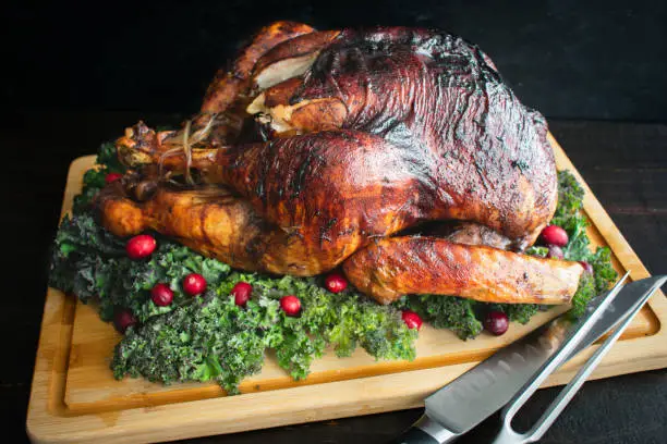A whole turkey on a bamboo carving board garnished with kale and cranberries