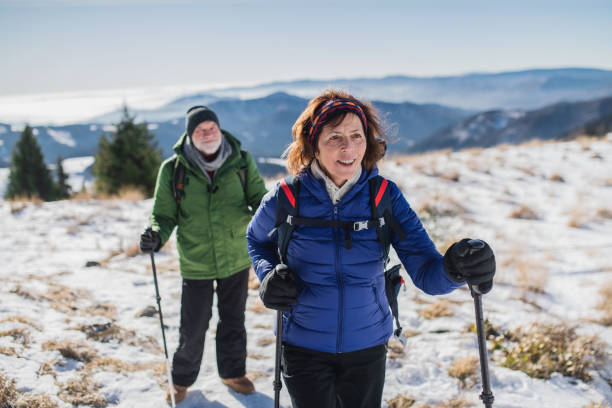 눈 덮인 겨울 자연에서 하이킹을 하는 북유럽 워킹 폴을 곁들인 시니어 커플. - winter hiking 뉴스 사진 이미지