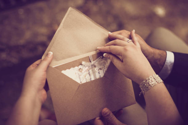 las manos de una pareja nupcial abren su invitación de boda en un tono vintage - invitación de boda fotografías e imágenes de stock