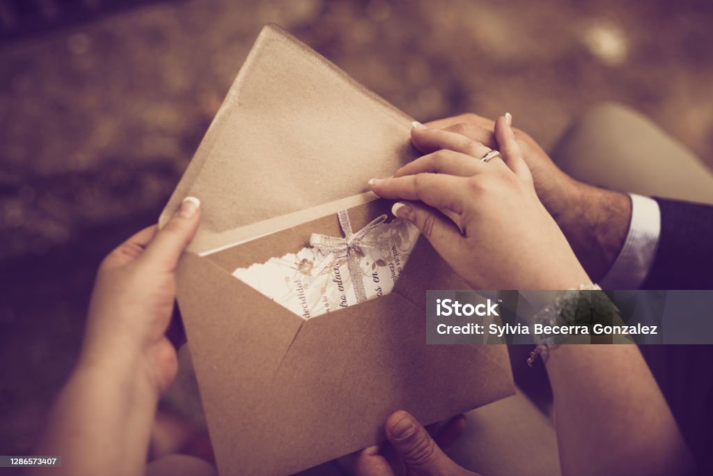The hands of a bridal couple open their wedding invitation in a vintage tone Wedding Invitation Stock Photo