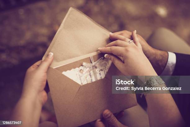The Hands Of A Bridal Couple Open Their Wedding Invitation In A Vintage Tone Stock Photo - Download Image Now