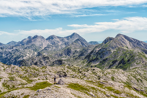 Men with arms raised in distance against high mountain range against  blue sky in Triglav national park.