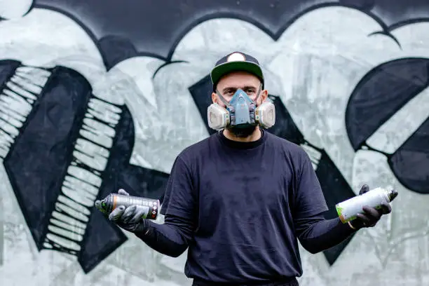 Photo of Graffiti artist posing in front of his drawing on the wall.