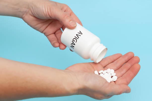 istock AVIGAN (Favipiravir) - White plastic packaging bottle in the hands with tablets. Isolated on blue background. Treatments for Coronavirus (COVID-19) 1286577290