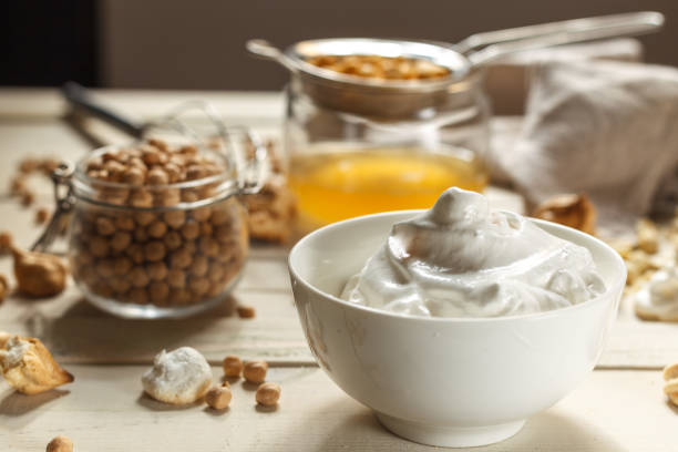 whipped soft meringue is aquafaba closeup and chickpeas in a glass jar. On a light wooden table. stock photo