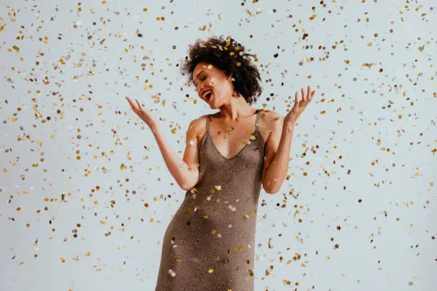 Photo of Party Time: Cheerful Young African American Woman Dancing in Confetti Rain (White Background)