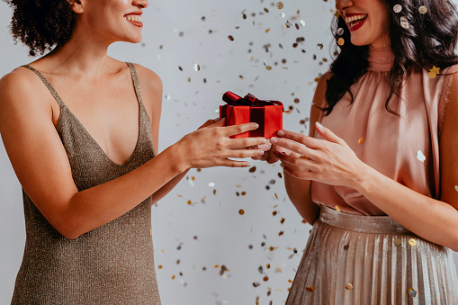 Two happy women surprising each other with Christmas gifts under confetti