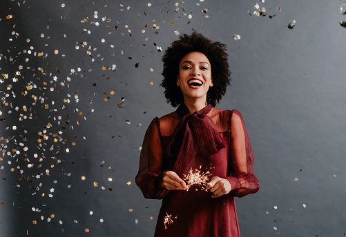 Studio shot of a beautiful elegant woman with an Afro haircut partying by holding lit sparklers in her hands