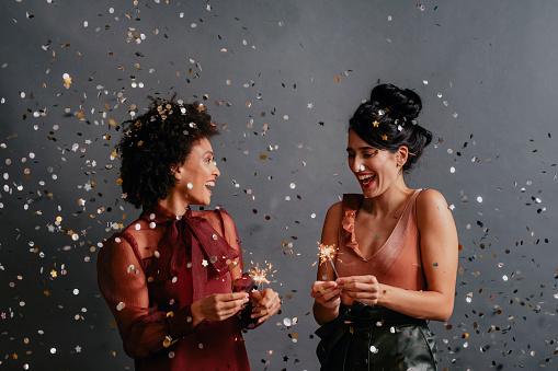 Two smiling women having a great time at a New Year's party (dark background)