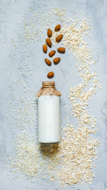 Milk in a bottle with a paper lid on a gray background with oatmeal, rice grains and nuts, top view stock photo