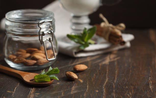 almonds in a small glass jar close up and a glass of milk on a dark background stock photo