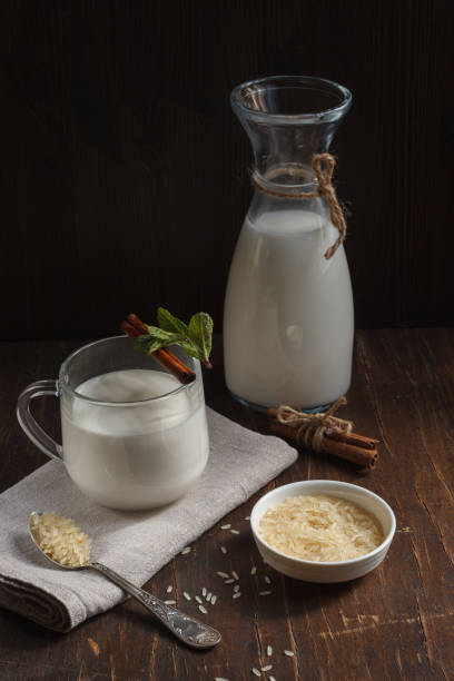 Rice vegetable milk in a Cup, a jug and white rice in a plate and a small spoon, vertically stock photo