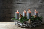 Rustic advent wreath of wood, fir branches and Christmas decoration with four burning candles against a gray wooden wall with copy space