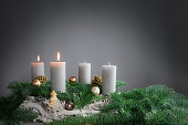Two of four candles are burning for the second Advent on fir branches with Christmas decoration against a grey background, copy space
