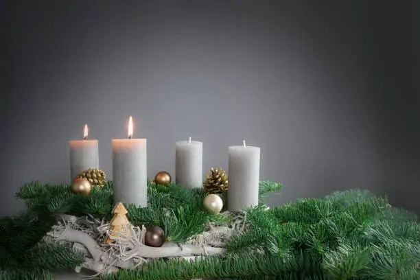 Two of four candles are burning for the second Advent on fir branches with Christmas decoration against a grey background, copy space, selected focus, narrow depth of field