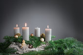 Three of four candles are burning for the third Advent on fir branches with Christmas decoration against a grey background, copy space