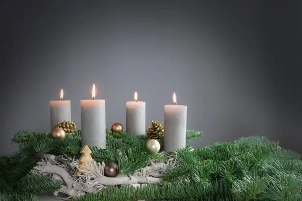 Four candles are burning for the fourth Advent on fir branches with Christmas decoration against a grey background, copy space, selected focus, narrow depth of field
