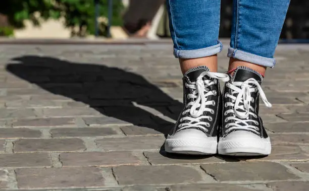 Image of  the lower part of teenager's legs in jeans and sneakers in a cobblestone street.