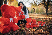 Beautiful woman with bunch of red teddy bears in park