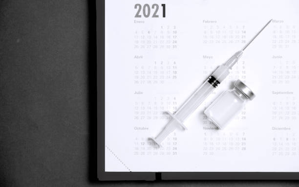 istock syringe and vaccine on calendar 2021 (black and white), black background 1286586874