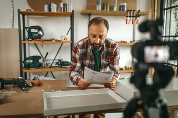 istock Mature man vlogging and explaining steps of making shelf from handbook 1286589729
