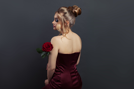 Beautiful woman profile and back head with blonde hairdo and red rose flower on black. Perfect model in red dress
