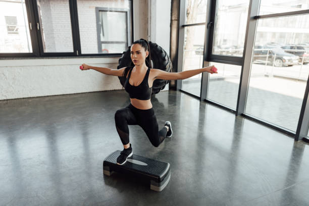 high angle view of sportswoman with dumbbells working out on step platform in gym - single step imagens e fotografias de stock