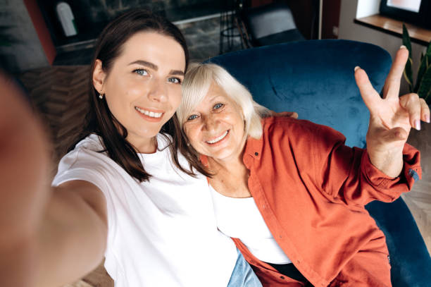 selfie avec grand-mère. la petite-fille adulte attirante prend un selfie sur un téléphone portable avec sa grand-mère grise âgée, ils sourient - wireless technology cheerful granddaughter grandmother photos et images de collection