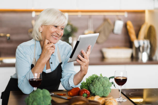 istock Smiling mature woman in apron standing in kitchen while cooking lunch or dinner and looking at recipe in her tablet 1286592016