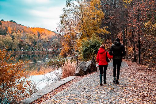 Sonbahar mevsiminde ormandaki göl kenarında yürüyen Çift. sevgililer yürüyüş yaparken arka taraftan göl manzarası ile birlikte fotoğraflanmışlardır.