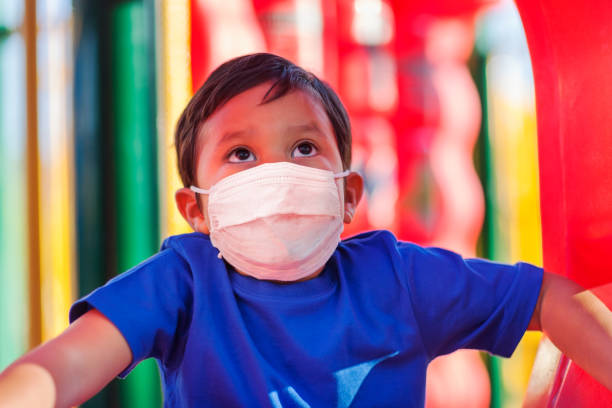 Little boy climbing into a kids playground while wearing a face mask to protect against viruses in public places. stock photo