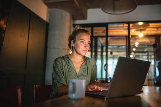 istock Blonde Businesswoman Using Laptop in Dimly Lit Board Room 1286598618