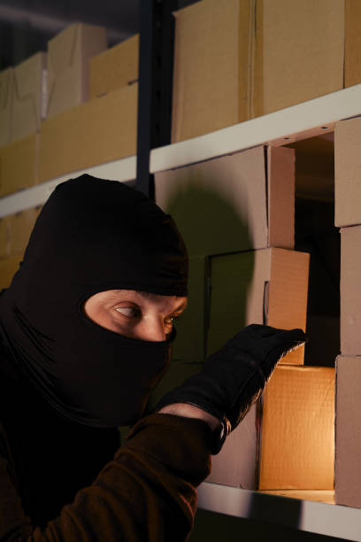 istock A man in a ski mask picks up a box with a parcel in a warehouse at night 1286598955